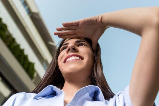 Successful Businesswoman standing on the street in front of Office Building and looking far away and covering sunlight his hand.