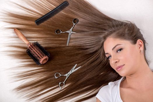 Cute young woman with beautiful healthy shiny hair and Haircutting Equipment.
