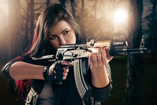 Attractive girl in forest standing in the attitude of aiming and looking through the sight automatic rifle.