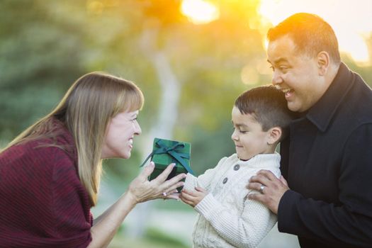 Happy Young Mixed Race Son Handing Gift to His Mom As Father Stands Behind.