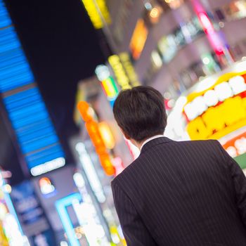 Solitary japanese corporative businessman in suit, after work, waiting on crossroad in Kabukicho, entertainment and red-light district in Shinjuku, Tokyo, Japan. 