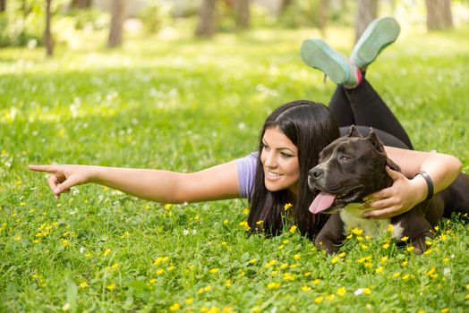 Beautiful young woman with her cute stafford terrier lying on grass in the park.