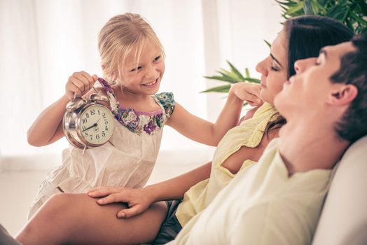 Cute little girl holding an alarm clock and waking up her parents