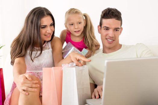 Beautiful happy family sitting at home with shopping bags and looking at laptop.