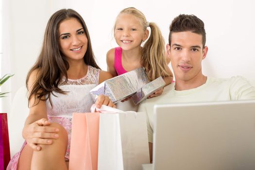 Beautiful happy family sitting at home with laptop and shopping bags. Looking at camera.