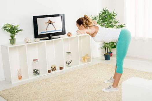 Beautiful girl doing stretching exercises at home in front of the tv