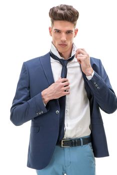 Serious young man looking at camera and doing his tie. White background.