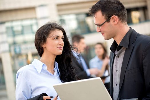 Young businessman talking to his business partner in front of office building and holding a laptop.