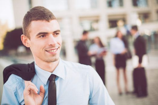 Portrait of a young smiling businessman standing in front of office building separated from the rest of the business team.