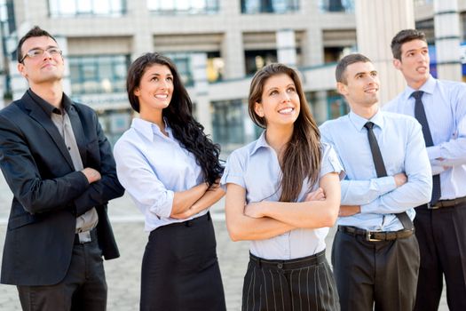 A small group of young business people standing in front of office building with arms crossed and with a smile on their faces looking in height.