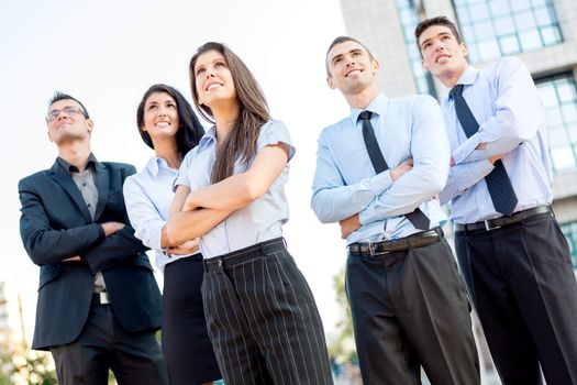 A small group of young business people standing in front of office building with arms crossed and with a smile on their faces looking in height.