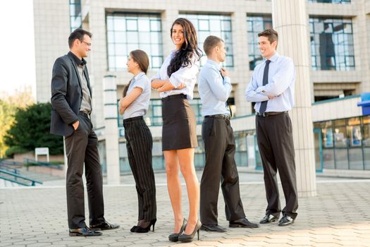 Cute young businesswoman with her team young business people standing in front of office building.