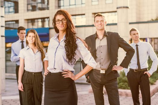 Beautiful young businesswoman with glasses standing proudly with his young colleagues in front of the office building.