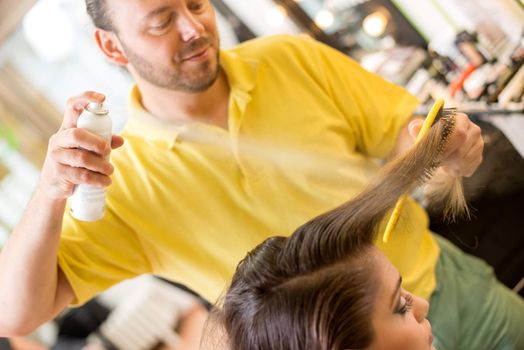 Man hairdresser spraying long brown hair of a customer woman.  