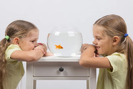 Two happy girls four and six years are at the table on which stands a fishbowl with goldfish