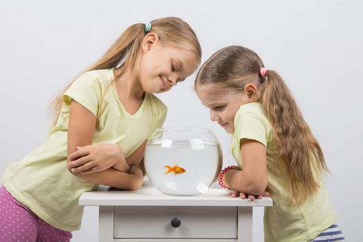 Two happy girls four and six years are at the table on which stands a fishbowl with goldfish