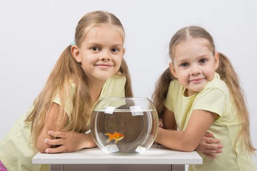 Two happy girls four and six years are at the table on which stands a fishbowl with goldfish