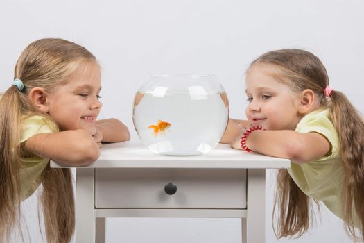 Two happy girls four and six years are at the table on which stands a fishbowl with goldfish