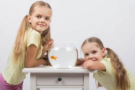 Two happy girls four and six years are at the table on which stands a fishbowl with goldfish