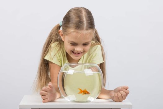 Happy six year old girl sits at a table at the fishbowl with goldfish