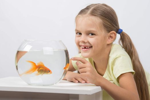 Happy six year old girl sits at a table at the fishbowl with goldfish