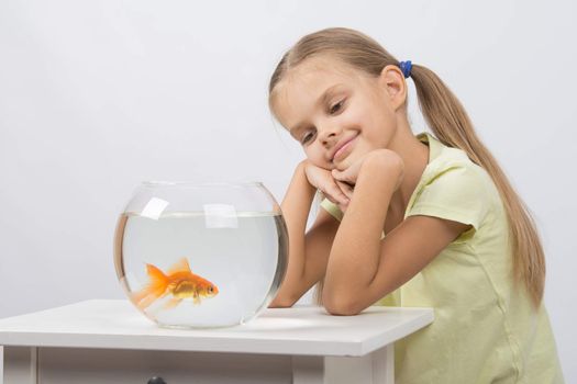 Happy six year old girl sits at a table at the fishbowl with goldfish