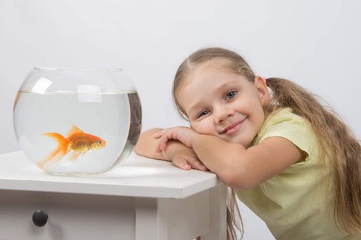 happy four-year girl sitting at a table near fishbowl with goldfish