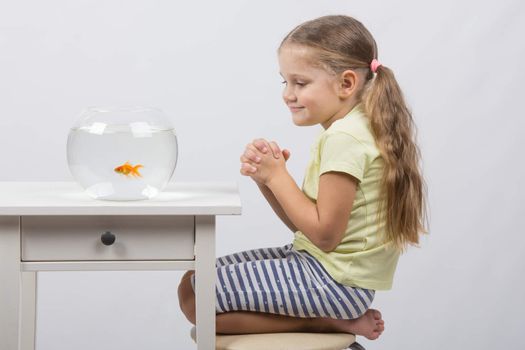 happy four-year girl sitting at a table near fishbowl with goldfish