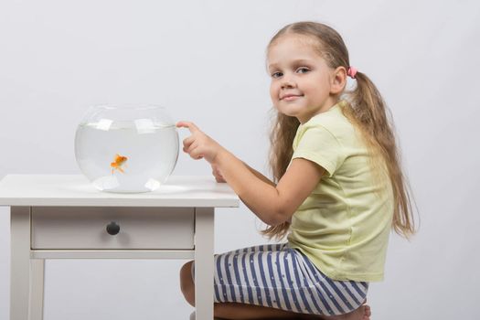 happy four-year girl sitting at a table near fishbowl with goldfish