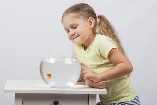 happy four-year girl sitting at a table near fishbowl with goldfish