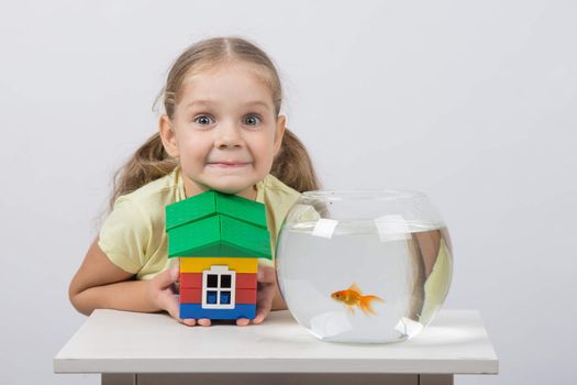 happy four-year girl sitting at a table near fishbowl with goldfish