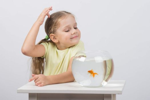 happy four-year girl sitting at a table near fishbowl with goldfish