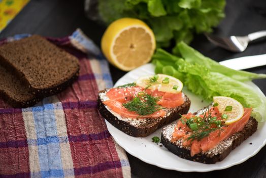 Homemade sandwich with salmon and rye bread , butter lemon, and lettuce for breakfast