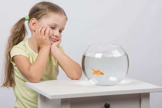 happy four-year girl sitting at a table near fishbowl with goldfish