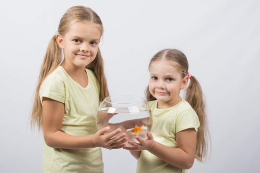 Two happy girls four and six years are holding fishbowl with goldfish