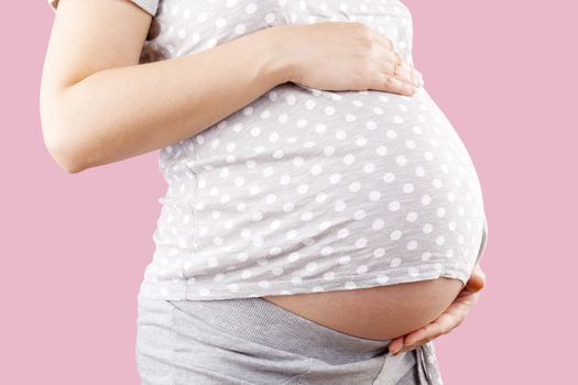 Pregnant beautiful woman touching big belly isolated on pink background. Pregnancy and motherhood. 