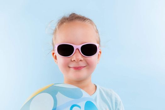 Summer. Adorable beautiful girl with ball and sunglasses against blue background. Summer background.