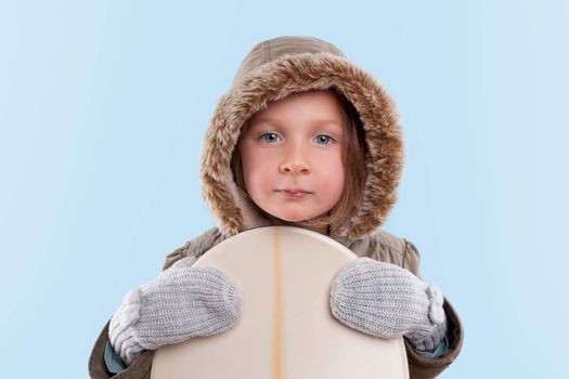 Little snowboarder. Cute little girl holding snowboard against light blue background. 