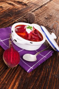 Delicious ukrainian borsch soup with fresh beetroot vegetable on purple cloth on rustic wooden table. Traditional european cuisine.