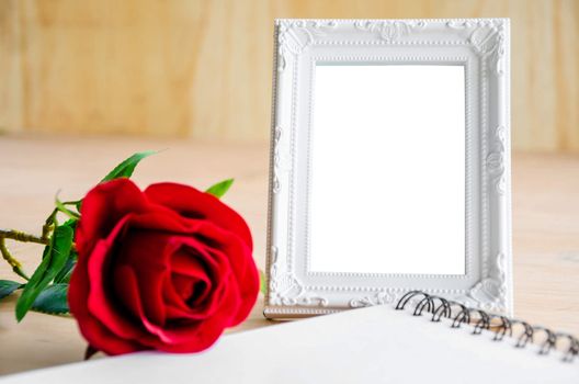 White vintage photo frame and red rose with open diary on wooden background. Save with clipping path.