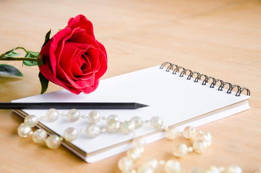 Focus red rose with blank diary on wooden background.