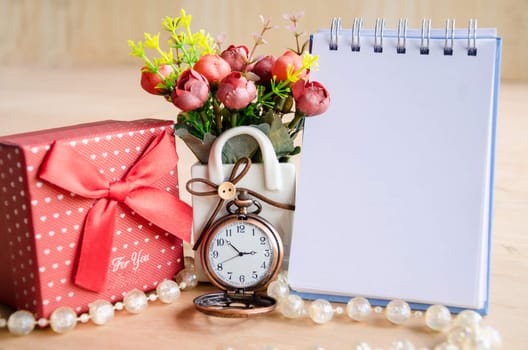 Diary, pocket watch, red gift box and flower on wooden background.