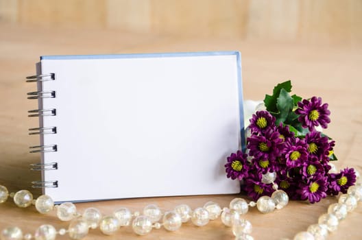 Blank diary and violet flower on wooden background.