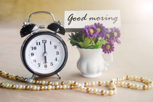 Alarm clock and Good morning tag with violet flower on wooden background.