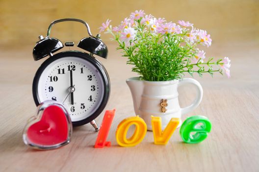 Pink flower and alarm clock on wooden background.