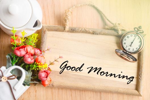 Good morning text in blank wooden photo frame with flower on wooden background.