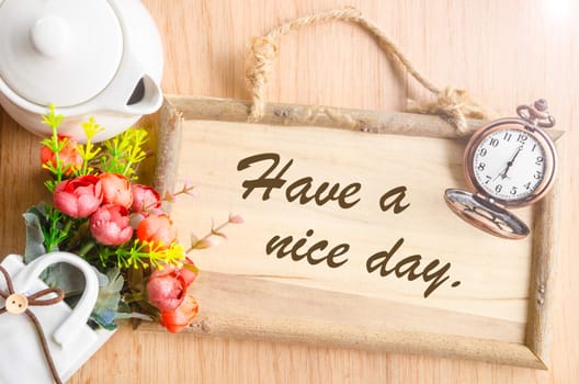 Have a nice day text in blank wooden photo frame with flower on wooden background.