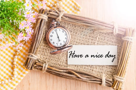 Have a nice day card and pocket watch at 6 AM with flower on wooden background.