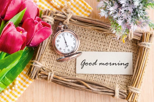 Good morning tag on sack photo frame with pocket watch and red tulip on wooden background.