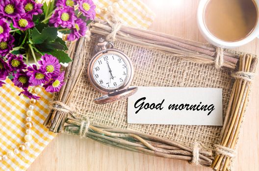 Good morning word on tag paper, pocket watch, violet flower and coffee in cup on wooden background.